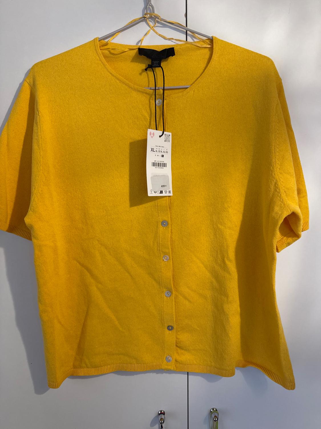Short-sleeved yellow cardigan hanging on a hanger, with a visible label indicating size XL. White background.