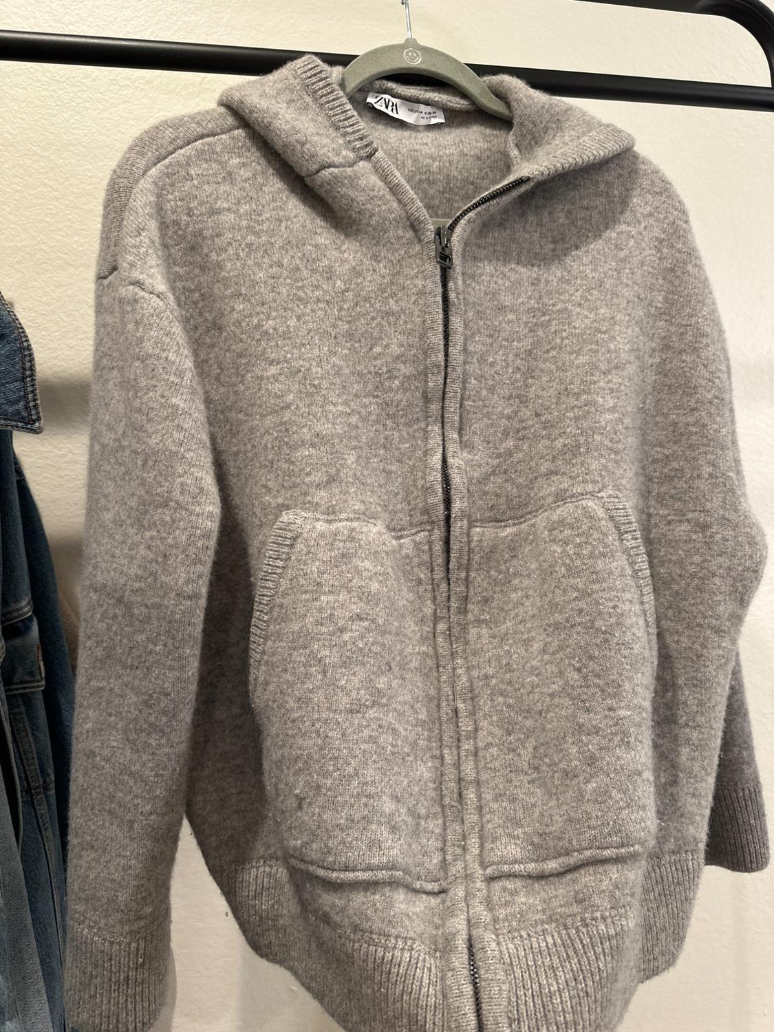 Front view of a grey zip-up hoodie with a hood, front pockets and ribbed cuffs.