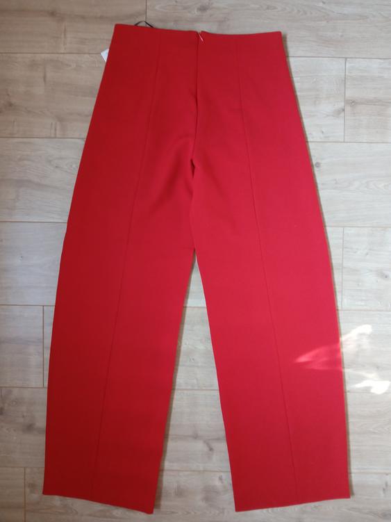 Red wide-leg trousers on a light wooden floor, viewed from above.