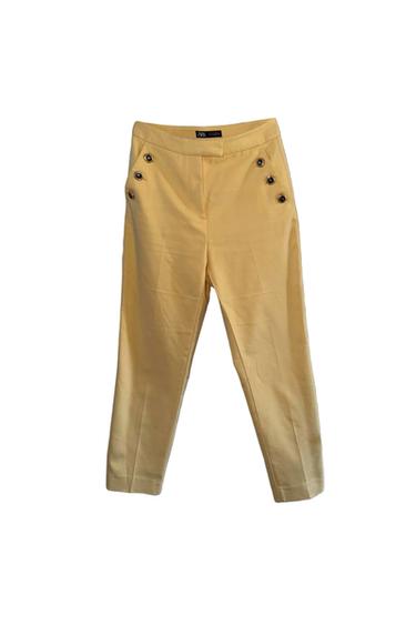 Yellow trousers with decorative buttons on the front pockets. Visible label on the waistband. White background.