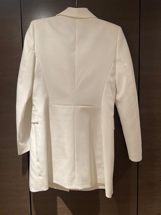 White jacket hanging on a hanger, viewed from behind, against a dark wooden background.