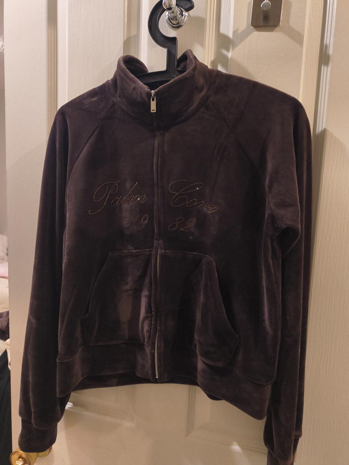 Brown velvet jacket hanging on a white door, with a zip and "Palm Cove 1982" text embroidered on the chest.