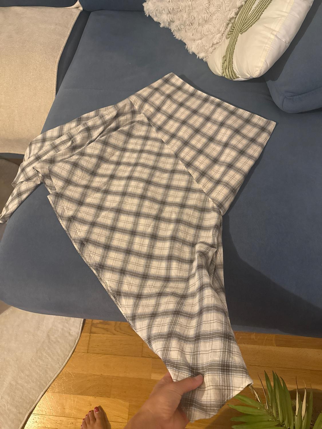 Someone is holding a checked garment over a blue sofa with cushions. Below, a wooden floor and a bare foot are visible.