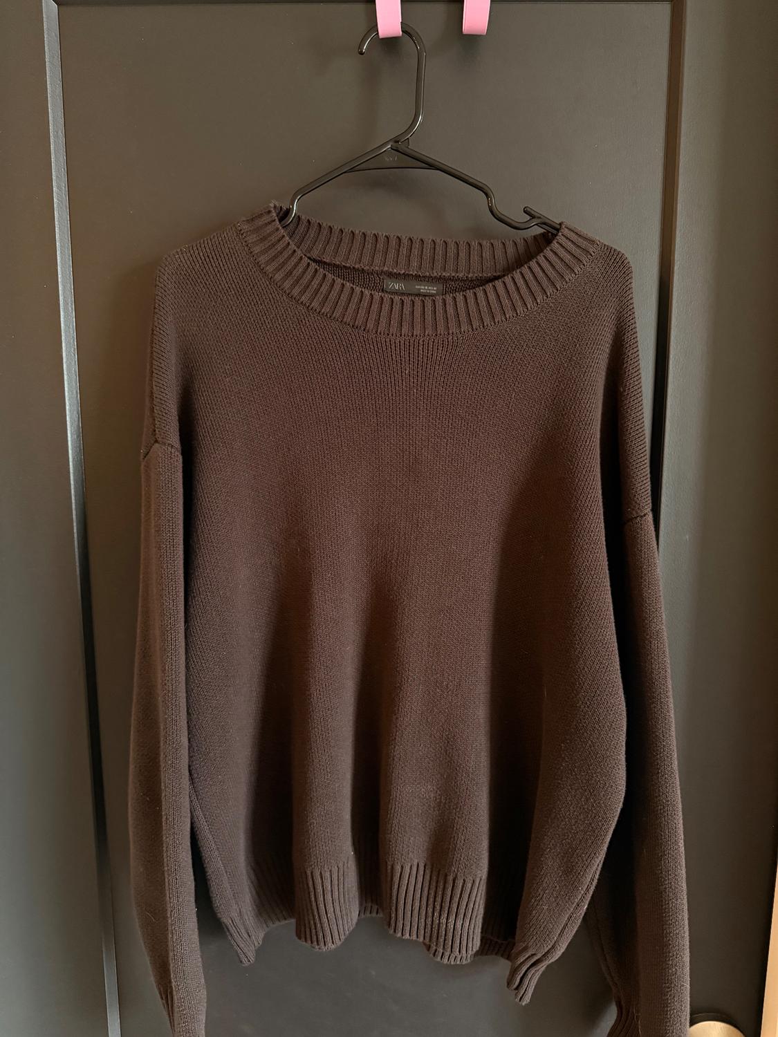 Brown knit sweater hanging on a black hanger with pink hooks, over a dark door.