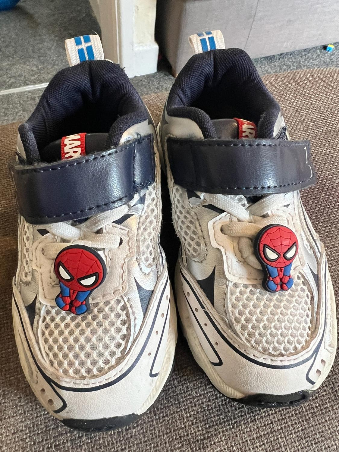 White and navy children’s trainers with an adjustable strap, Spider-Man decoration and MARVEL label, on a fabric surface.