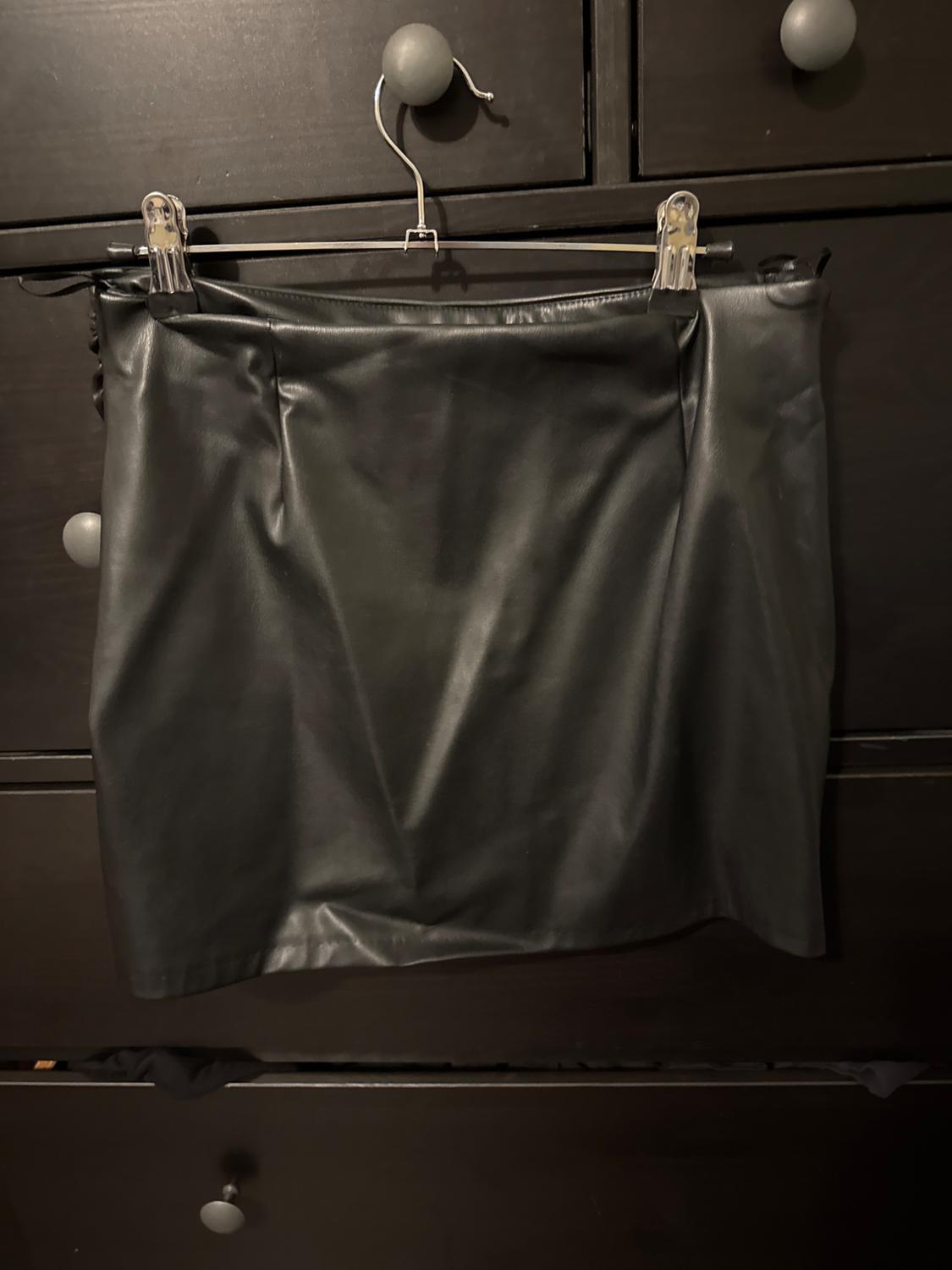 Black skirt hanging on a hanger in front of a dark cabinet with round gray handles.