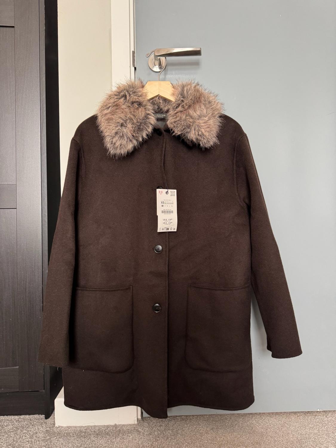 Brown coat with a faux-fur collar hanging on a door. Shows buttons, pockets and the text COLLECTION, XS, US $179, UK £119.