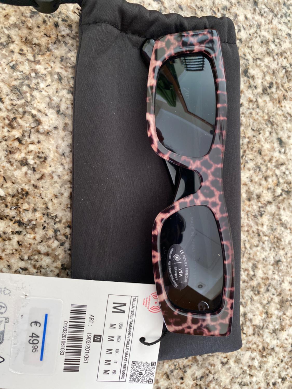 Sunglasses with a pink-toned patterned frame, in a black case. Label shows price of €49.95 and size M.
