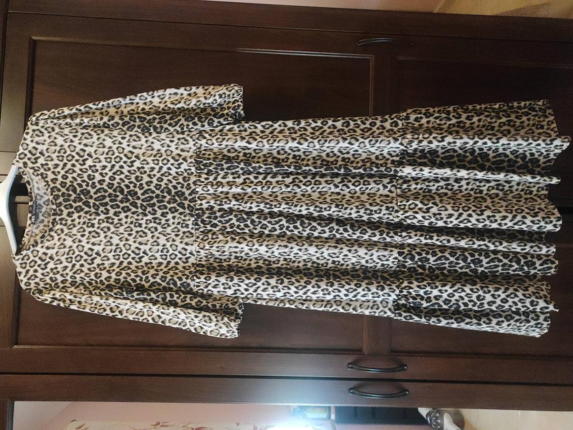 Long leopard print dress hanging on a hanger in front of a dark wooden wardrobe.