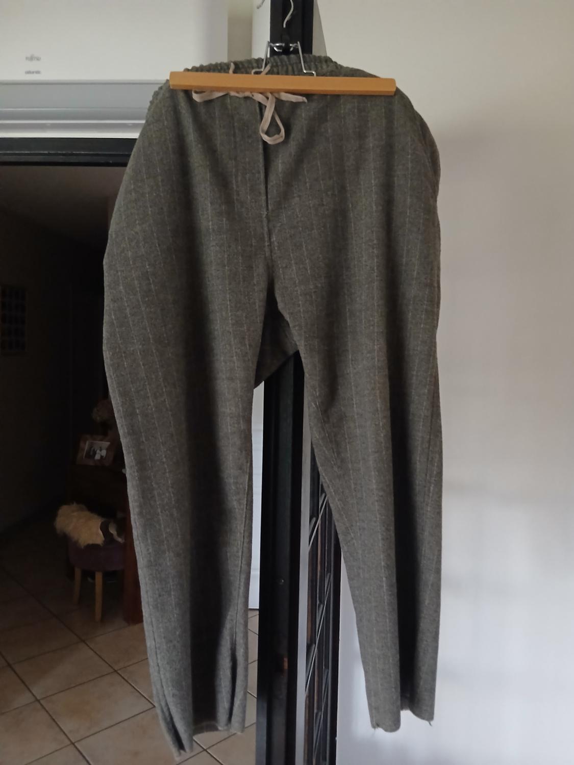 Grey fabric trousers with vertical stripes, hung on a wooden hanger, interior background of a house with a tiled floor.