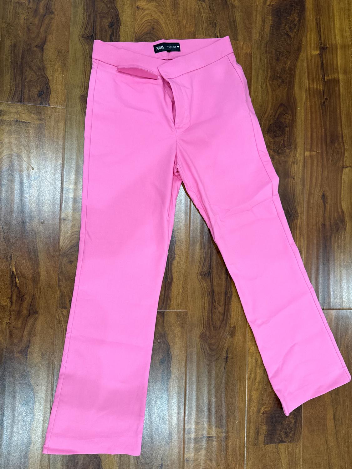 Pink, straight-leg trousers on a wooden floor. Label visible at the waist.