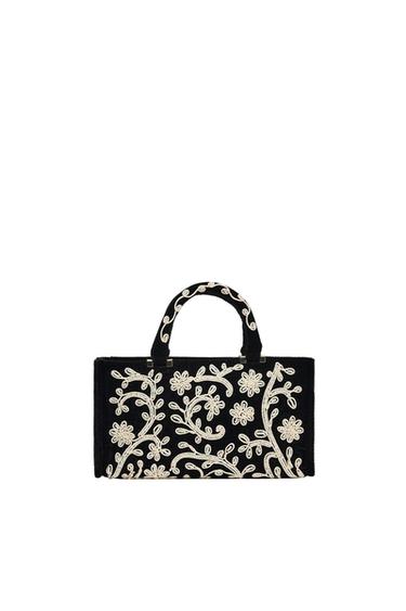 Black handbag with white spiral floral embroidery on a white background. Rectangular design with matching short handles.