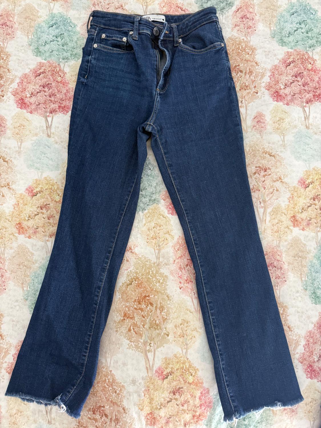 Τζιν παντελόνι Zara από μπλε σκούρο denim με ξέφτι στο τελείωμα, σε φόντο με μοτίβο από στυλιζαρισμένα δέντρα σε παστέλ αποχρώσεις.