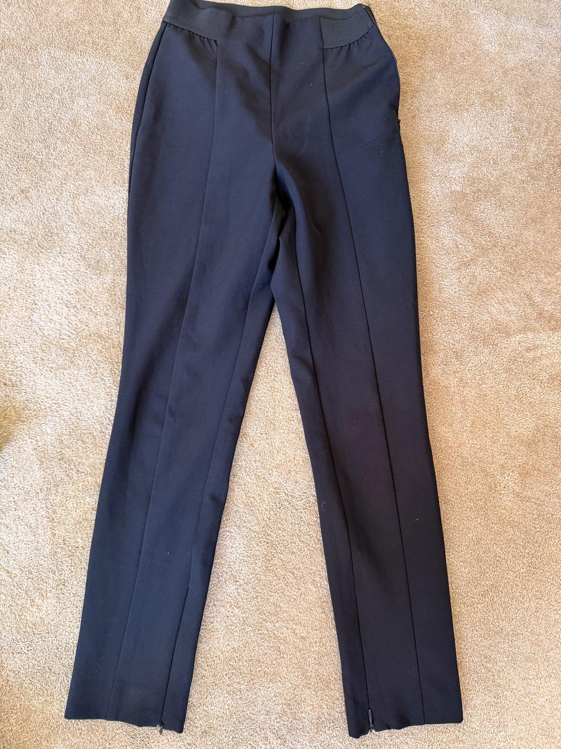 Plain black trousers with front pleats, placed on a beige rug.