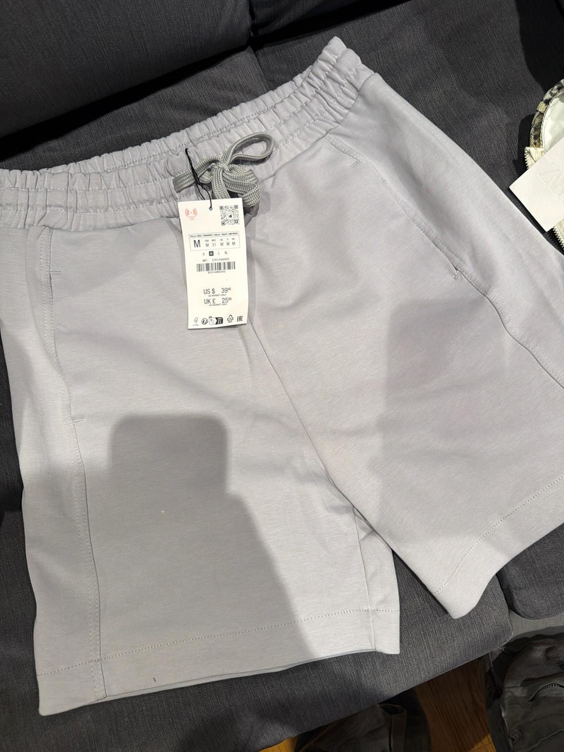 Light gray shorts with an elastic waistband and drawstring. Visible price label with size M, US $39.90 and UK £25.99.