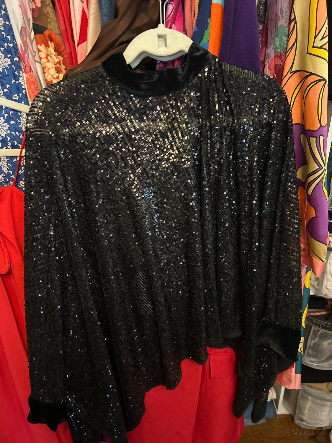 Black sequined blouse hanging in a closet full of colorful, patterned clothes, including florals and geometric designs.