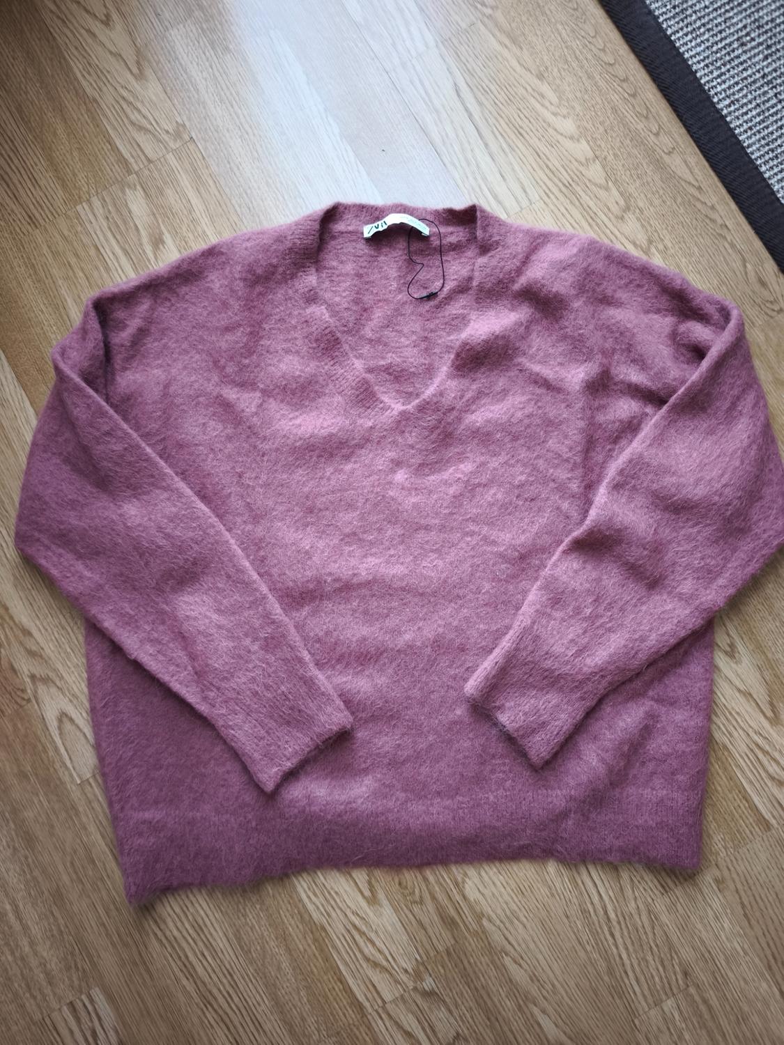 Pink wool V-neck long-sleeved jumper, placed on a light wooden floor. Label visible on the collar.