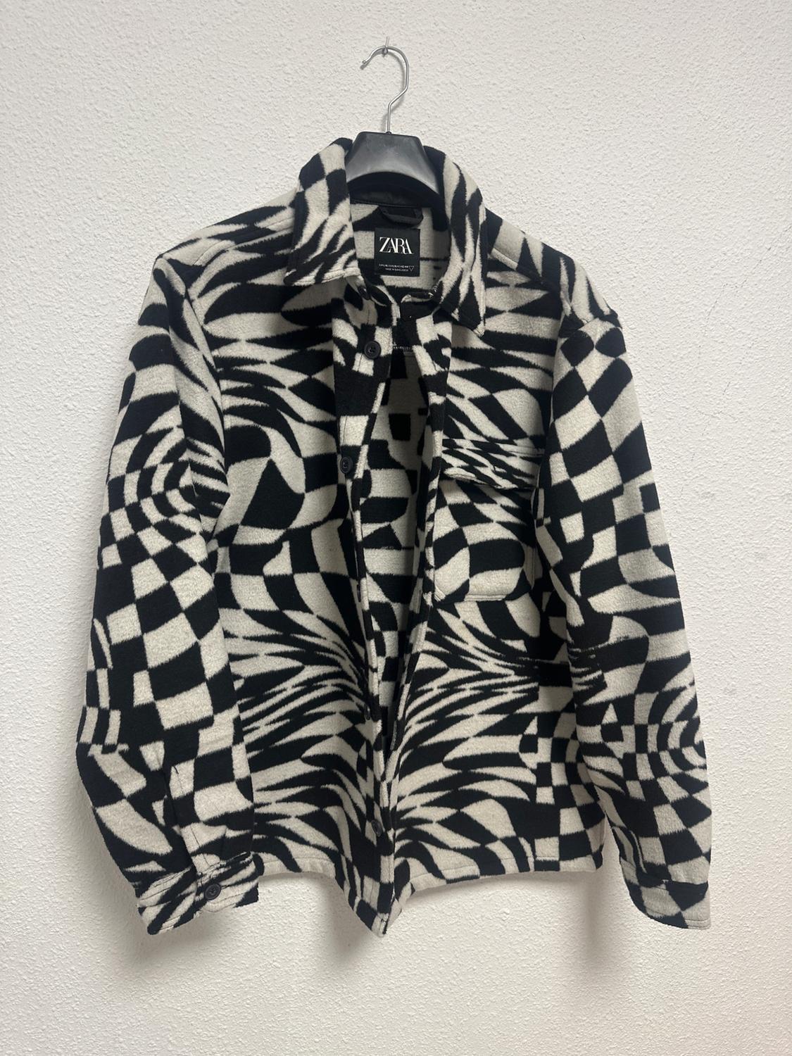 Jacket hanging with a black and white geometric print. Visible label with the text "ZARA". White background.