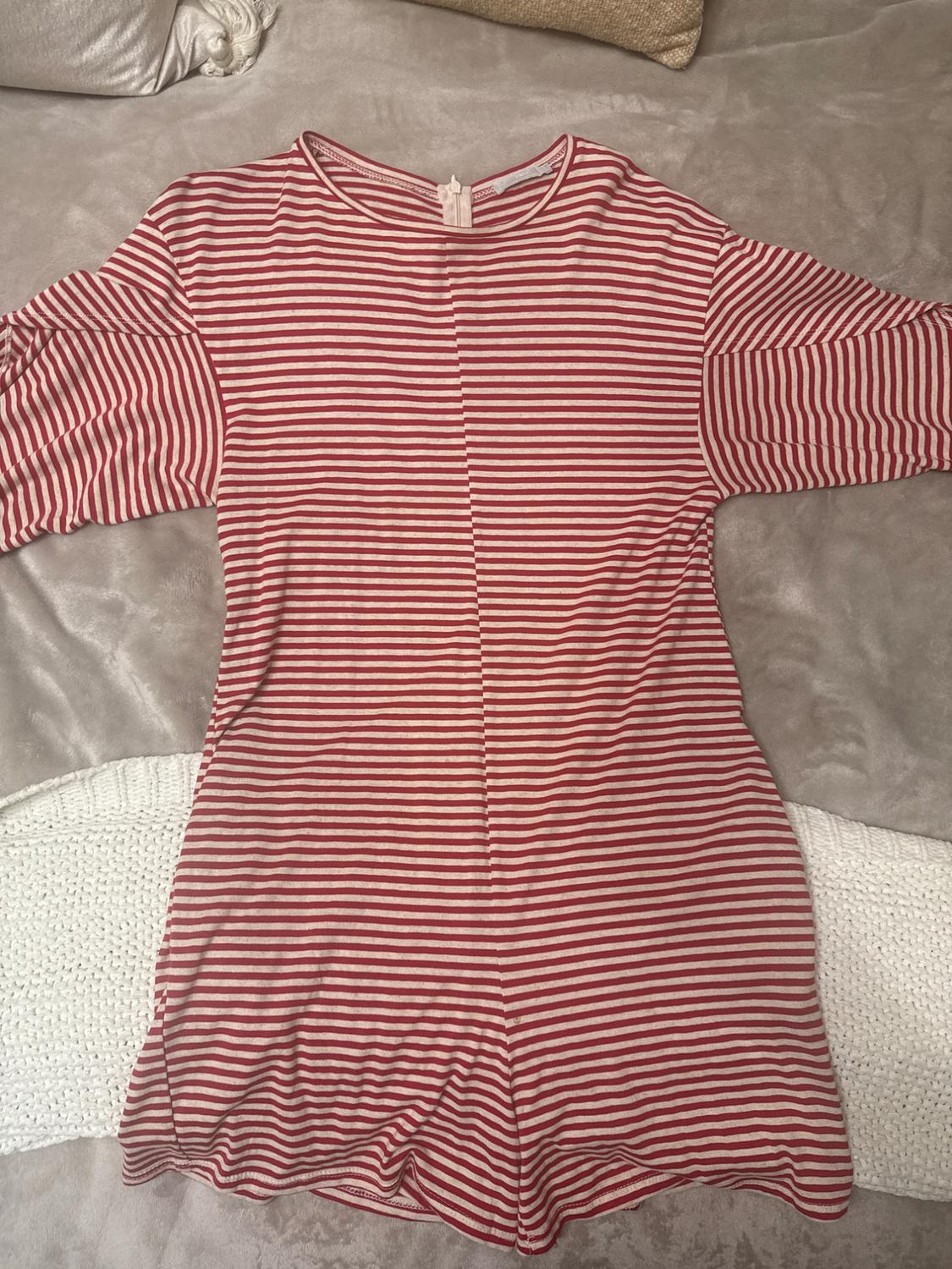Red and white striped dress with long sleeves, spread out on a gray surface. Background with light-colored cushions.