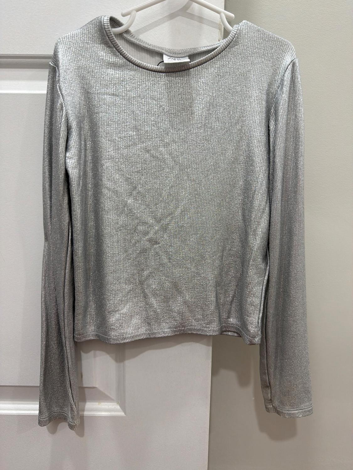 Light gray long-sleeved jersey hanging on a white hanger over a white door. Ribbed texture fabric.