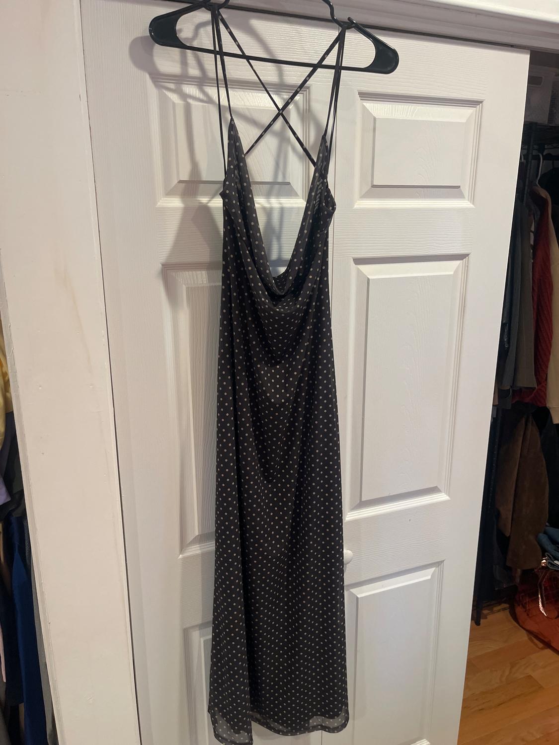 Black, thin-strapped dress with a white polka dot print, hanging on a hanger in front of a white door.