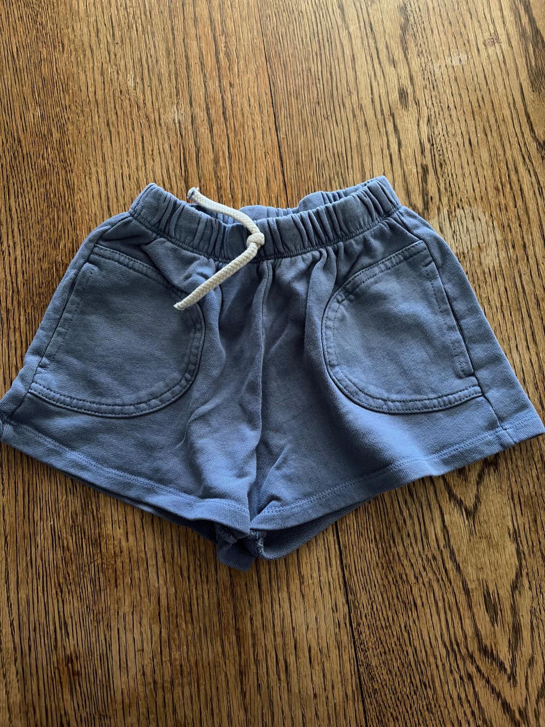 Blue shorts with an elasticated waist and white drawstring, on a wooden floor.