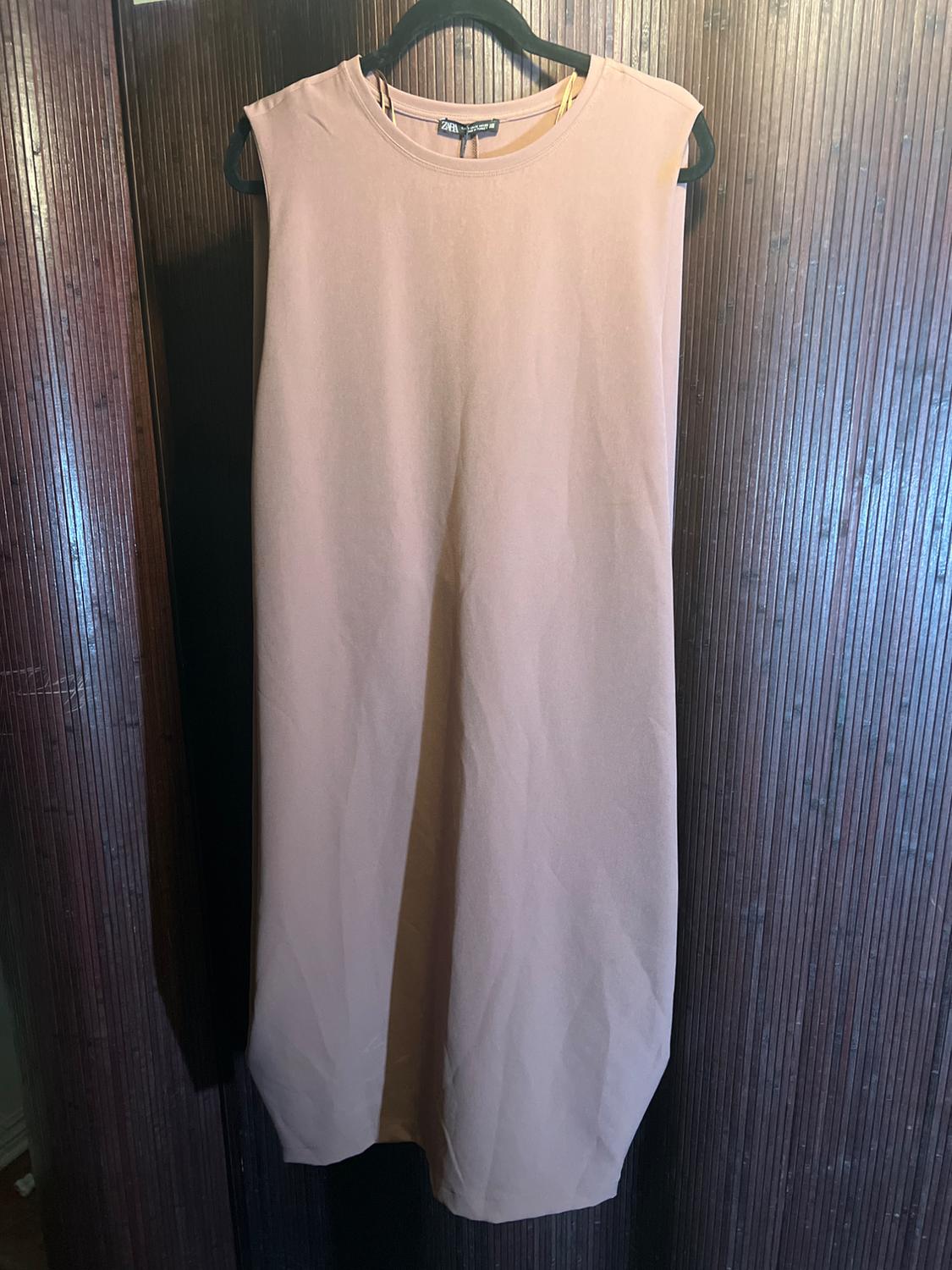 Beige sleeveless dress hanging on a black hanger against a dark wood panel background.