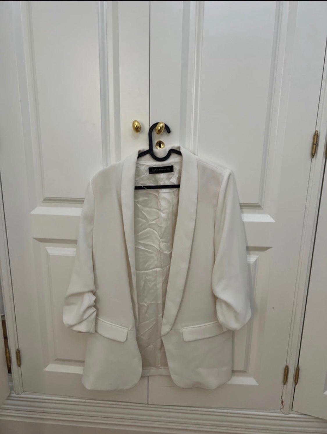 White blazer with gathered sleeves hanging on a white door with gold handles. Internal label with the text ZARA WOMAN.