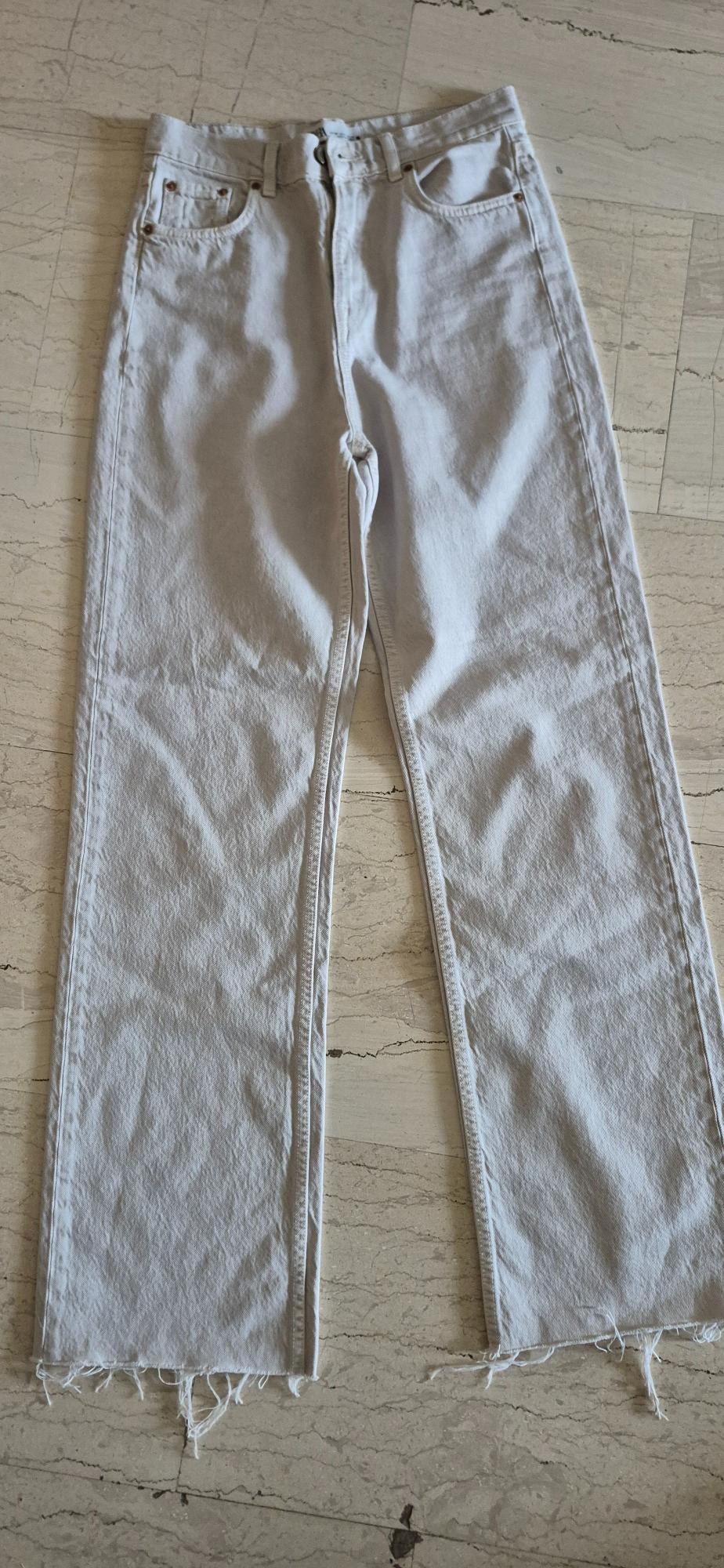 White denim jeans with a frayed hem, placed on a light marble floor.