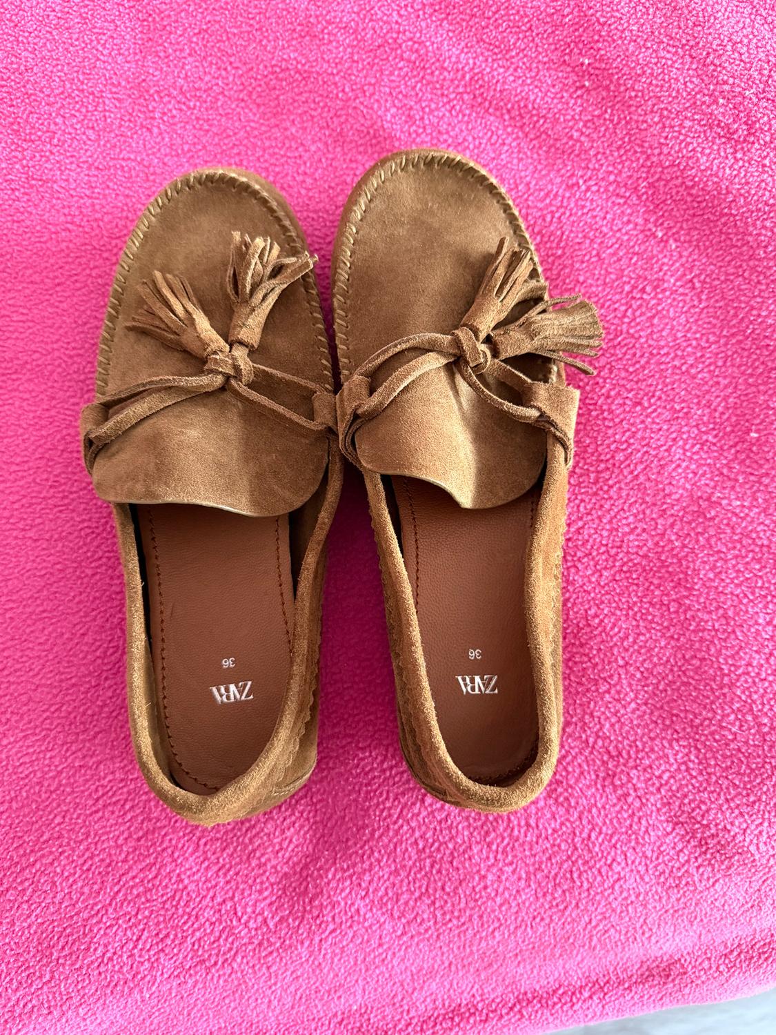 Brown loafers with bow and tassels on pink fabric. Interior with "ZARA" logo and size "36".