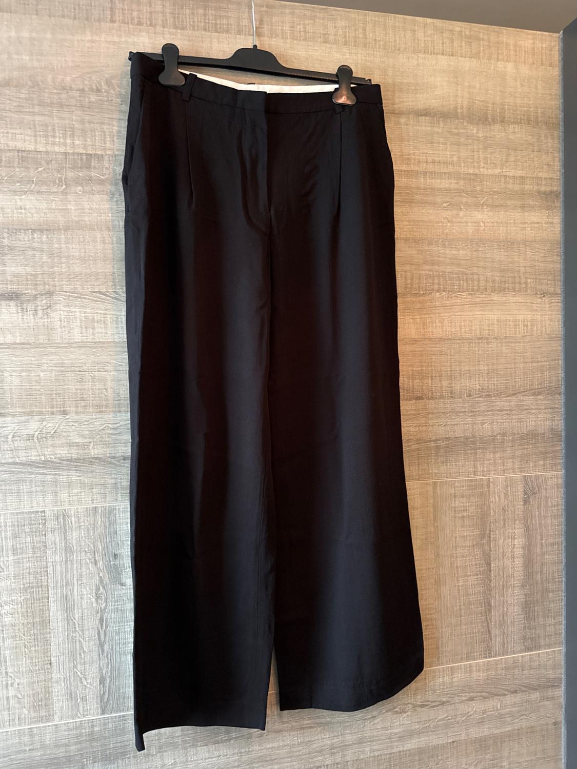 Black wide-leg trousers hanging on a black hanger against a light wooden background.