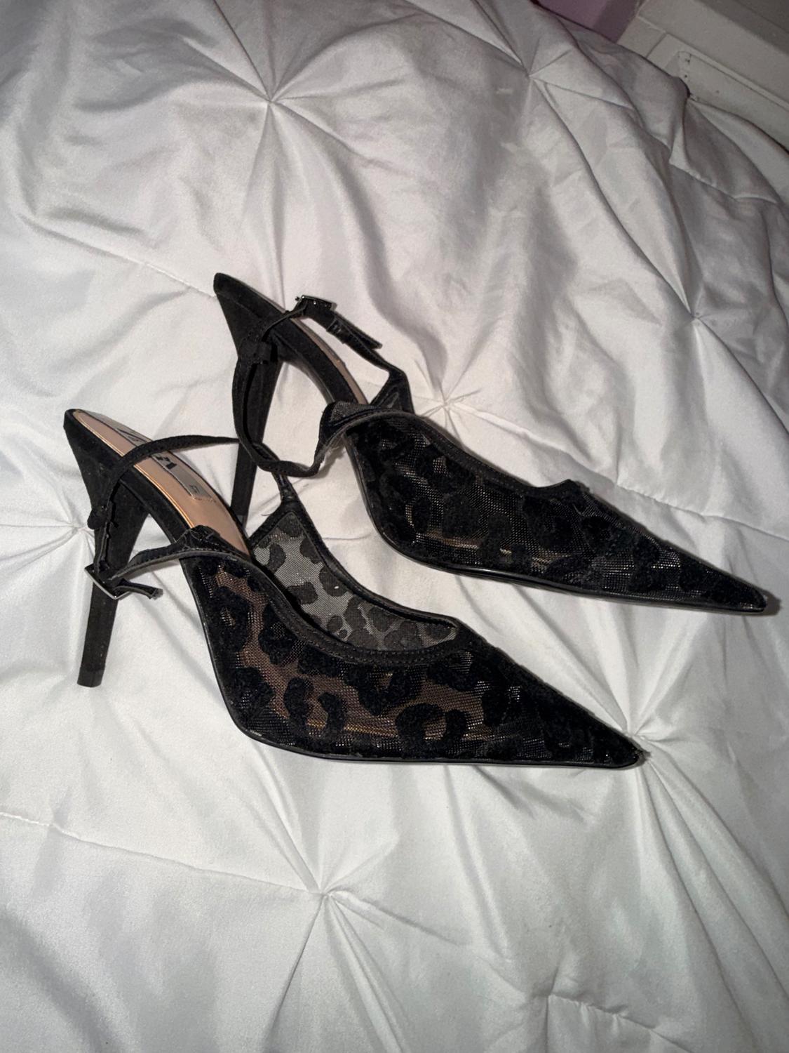 Black high heels with leopard print on a quilted white bedspread.