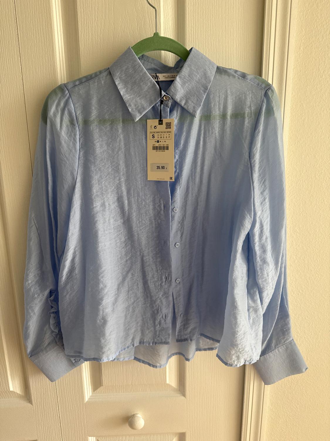 Light blue long-sleeved shirt hanging on a green hanger. Visible tag with a price of 35.90. White door background.