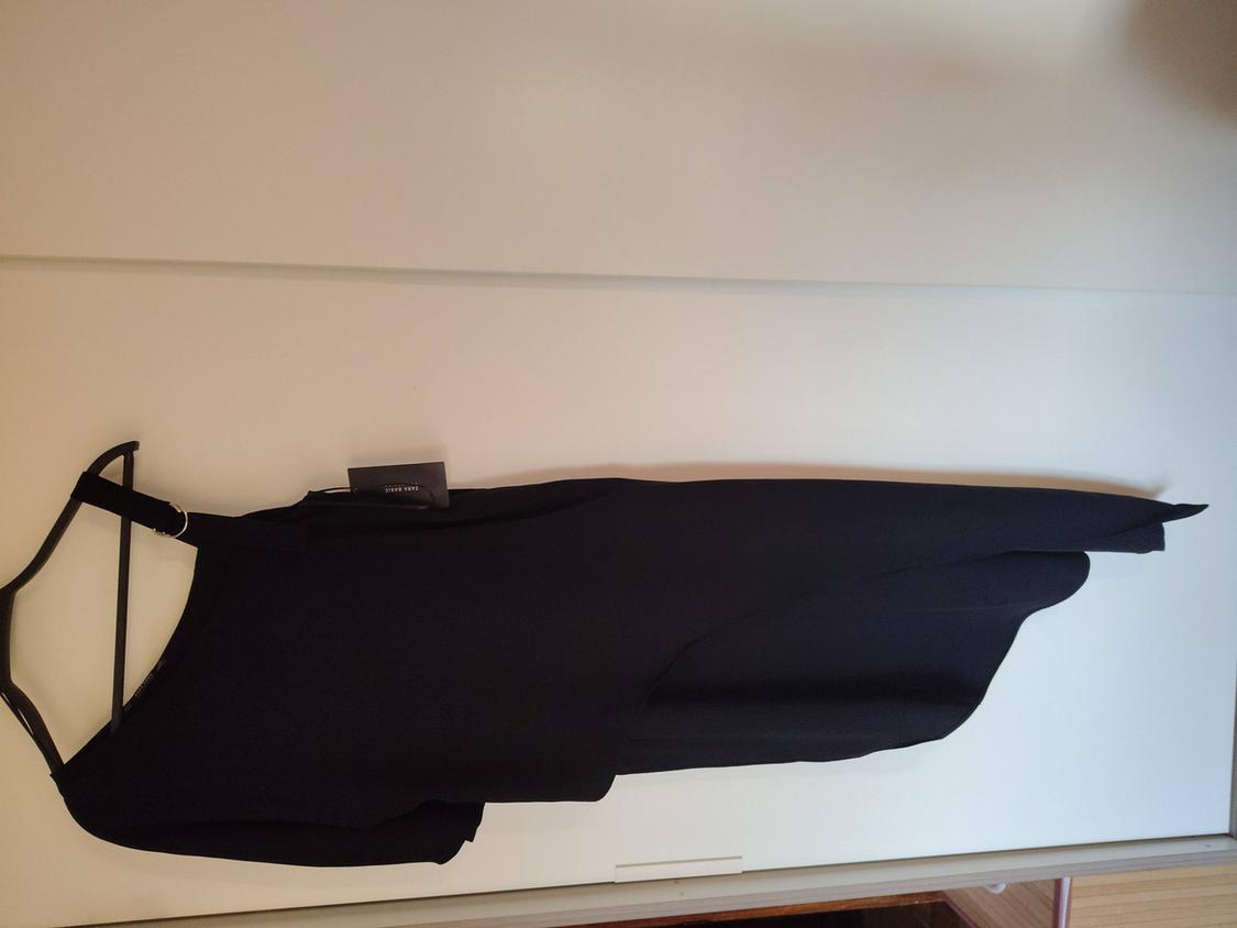 Asymmetric black dress hanging on a black hanger over a white door. Label visible on the dress's collar.