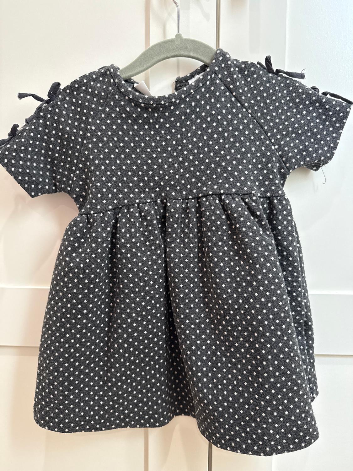 Grey children's dress with white polka dot print, short sleeves with bows, hanging on a grey hanger against a white background.
