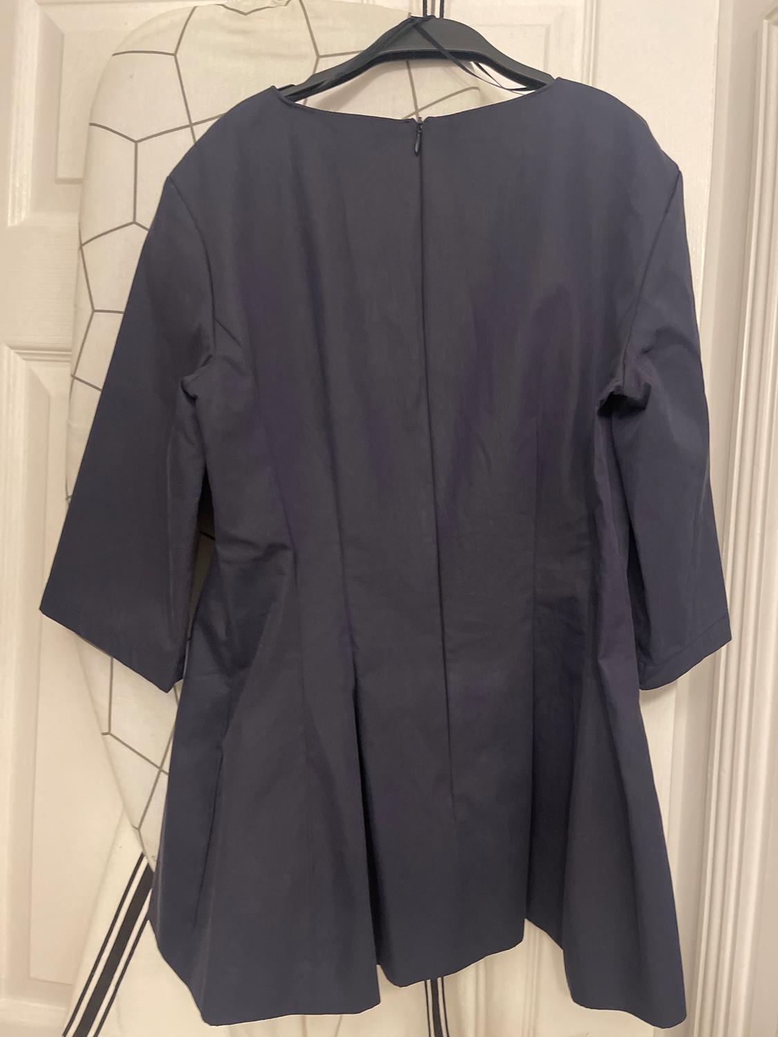 Dark blue, long-sleeved dress hanging on a hanger over an ironing board with a geometric design in the background.