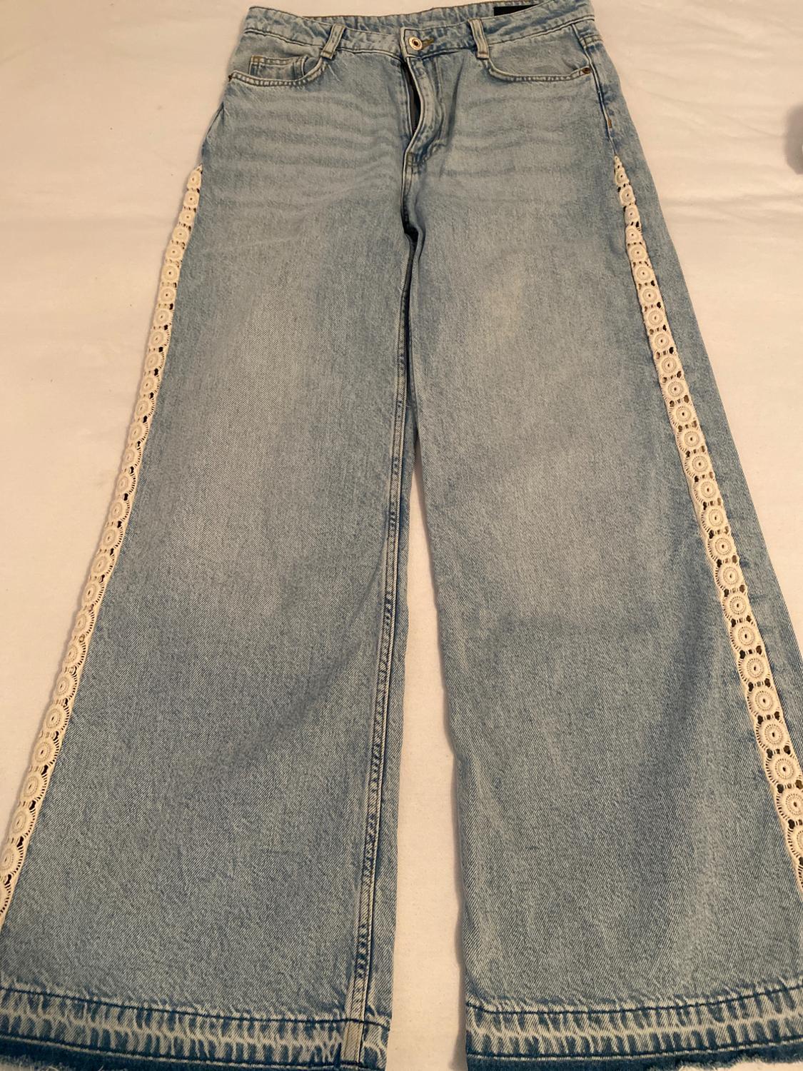 Light blue, wide-leg jeans with white lace side detailing and a frayed hem, spread out on a white surface.