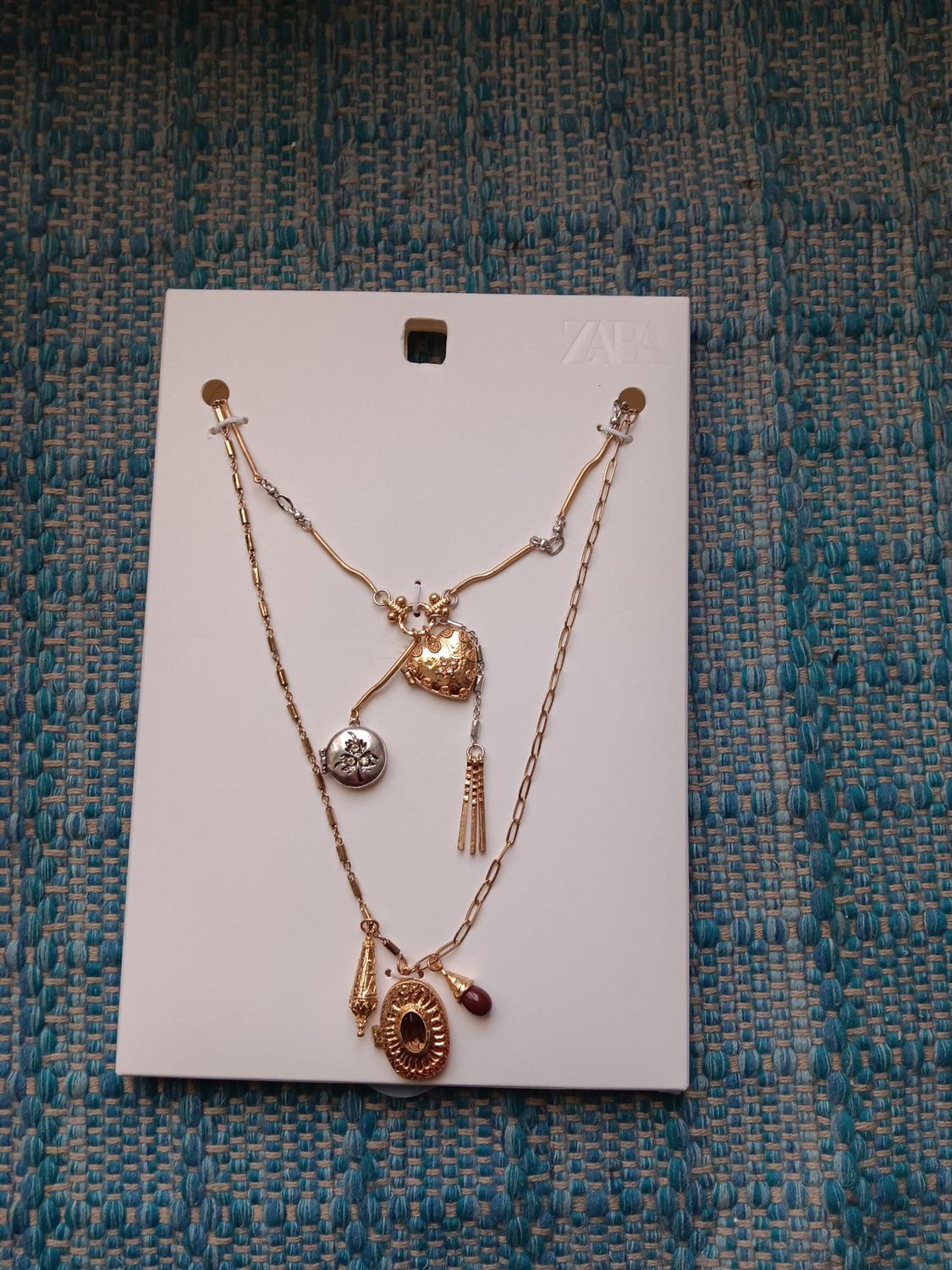 Gold necklace with decorative pendants on a white background, placed on a textured blue fabric surface.