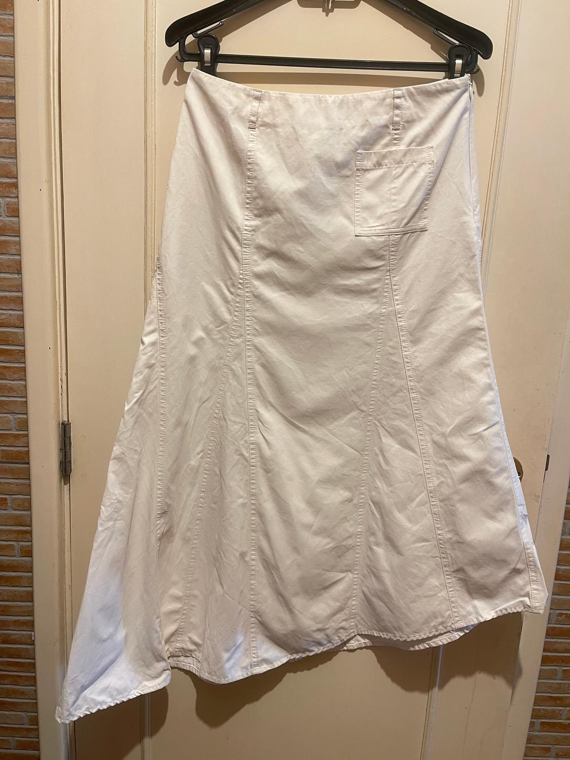 Asymmetric white skirt hanging on a black hanger over a light wooden door. Visible back pocket detail.