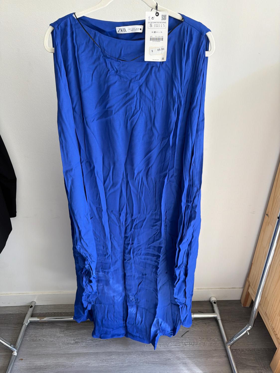 Creased blue dress hanging on a hanger with a price tag of 69.90. White background and grey wooden floor.