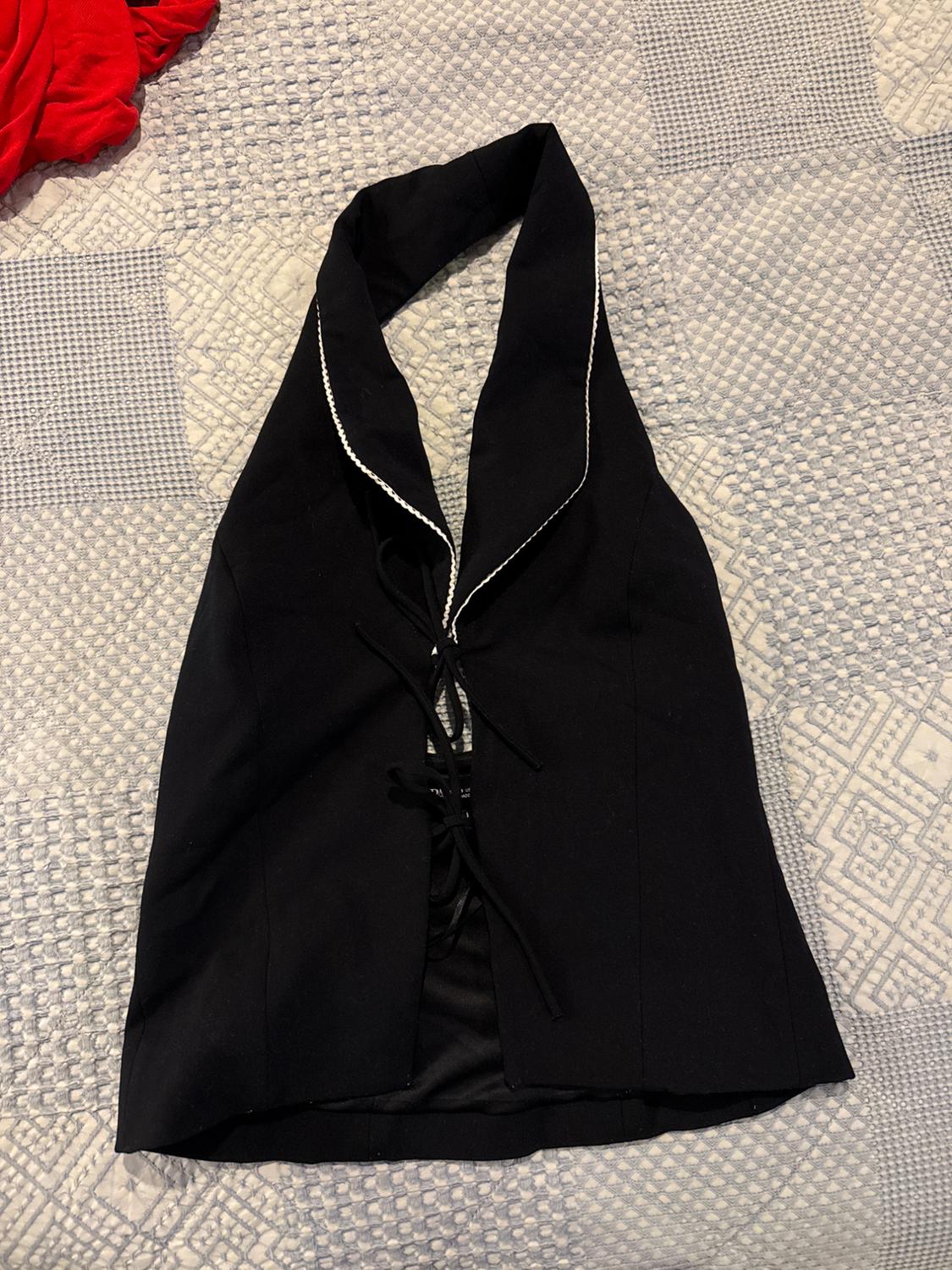 Black V-neck vest with front lacing, over a gray geometric pattern quilt. Red fabric visible on the left.