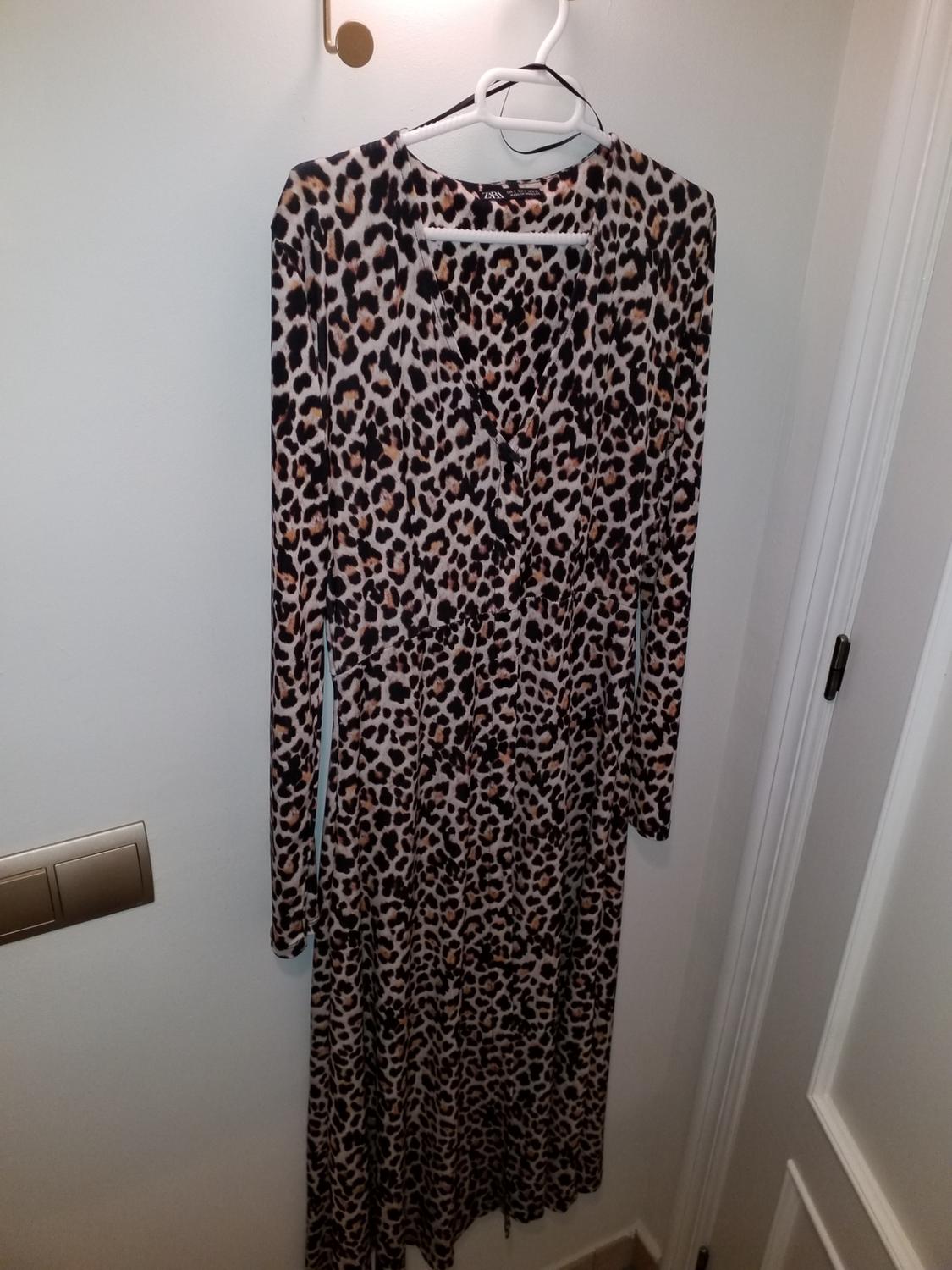 Animal print dress hanging on a white hanger against a light-coloured wall, with a light switch to the left.