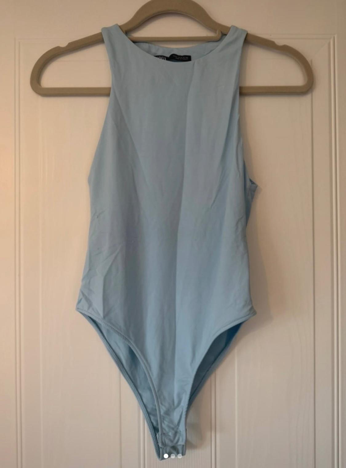 Light blue sleeveless bodysuit hanging on a coat hanger in front of a white door.