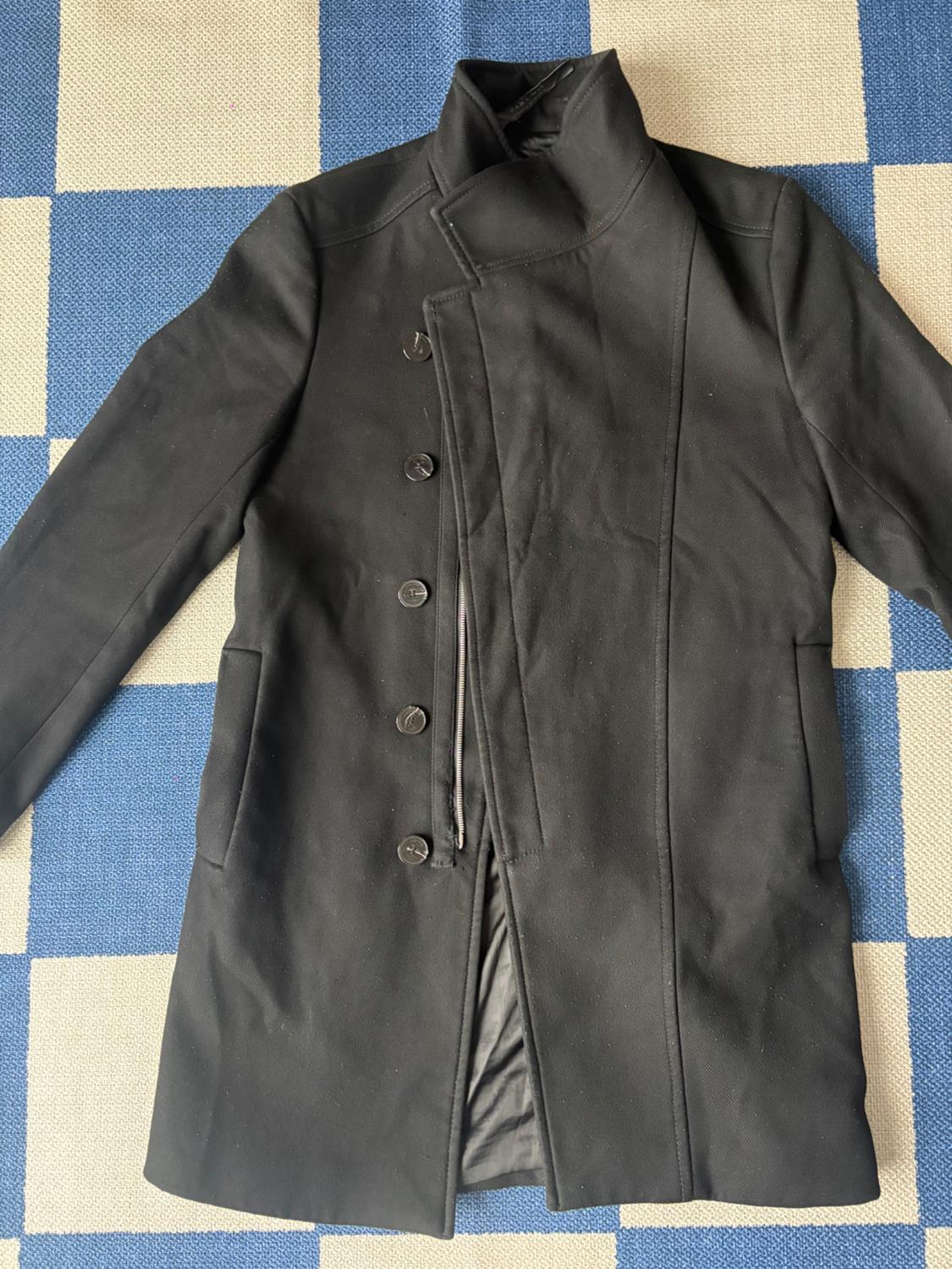 Black coat with a high collar and buttons, on a blue and white checkered rug. Elegant and modern design.