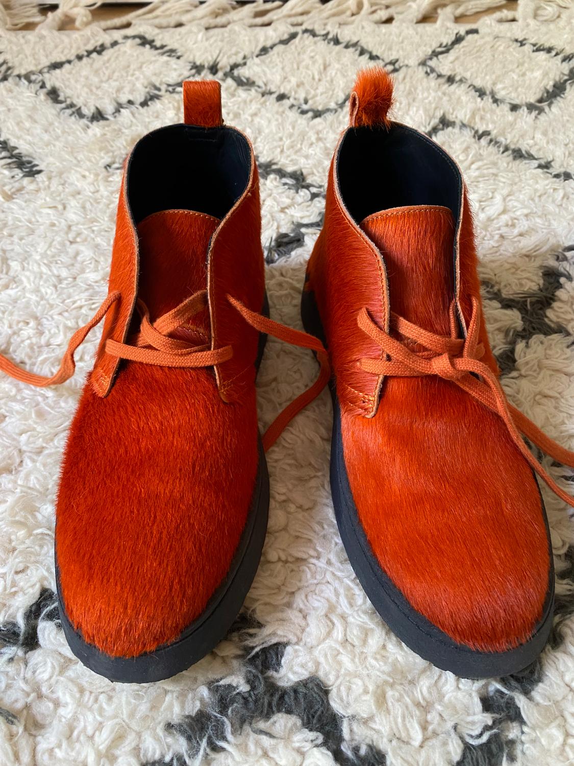 Orange fur boots with laces on a white rug with a black geometric design.