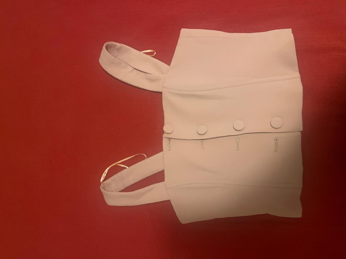 Beige cropped top with wide straps and fabric-covered buttons on the front, laid out on a red background.