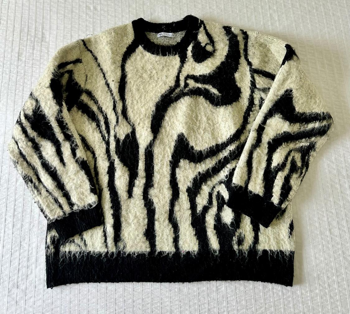 Wool jumper with abstract black and white design on a textured white surface.