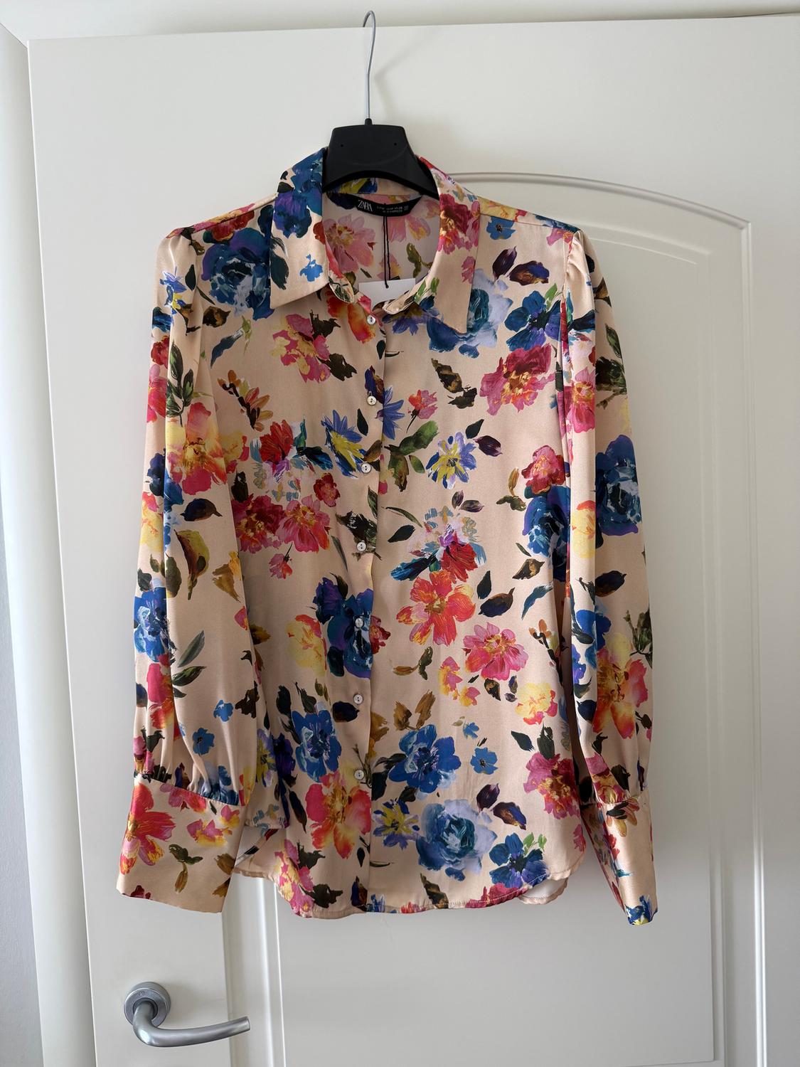 Long-sleeved shirt with a floral print in shades of blue, pink, and yellow, hanging on a hanger over a white door.