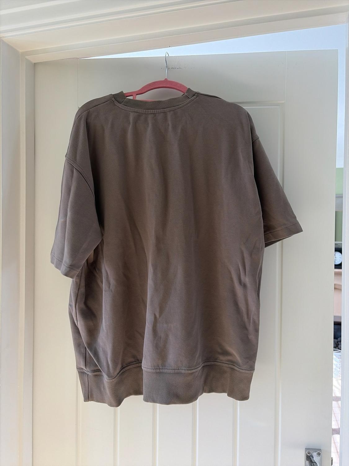 Brown short-sleeved, oversized sweatshirt hanging on a pink hanger
on a white, ajar door.