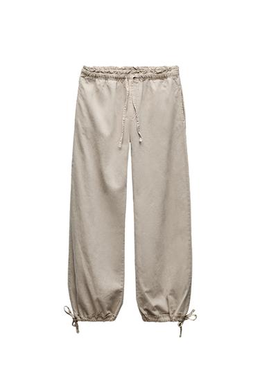 Front view of beige trousers with elasticated waistband and adjustable drawstrings at the ankles.